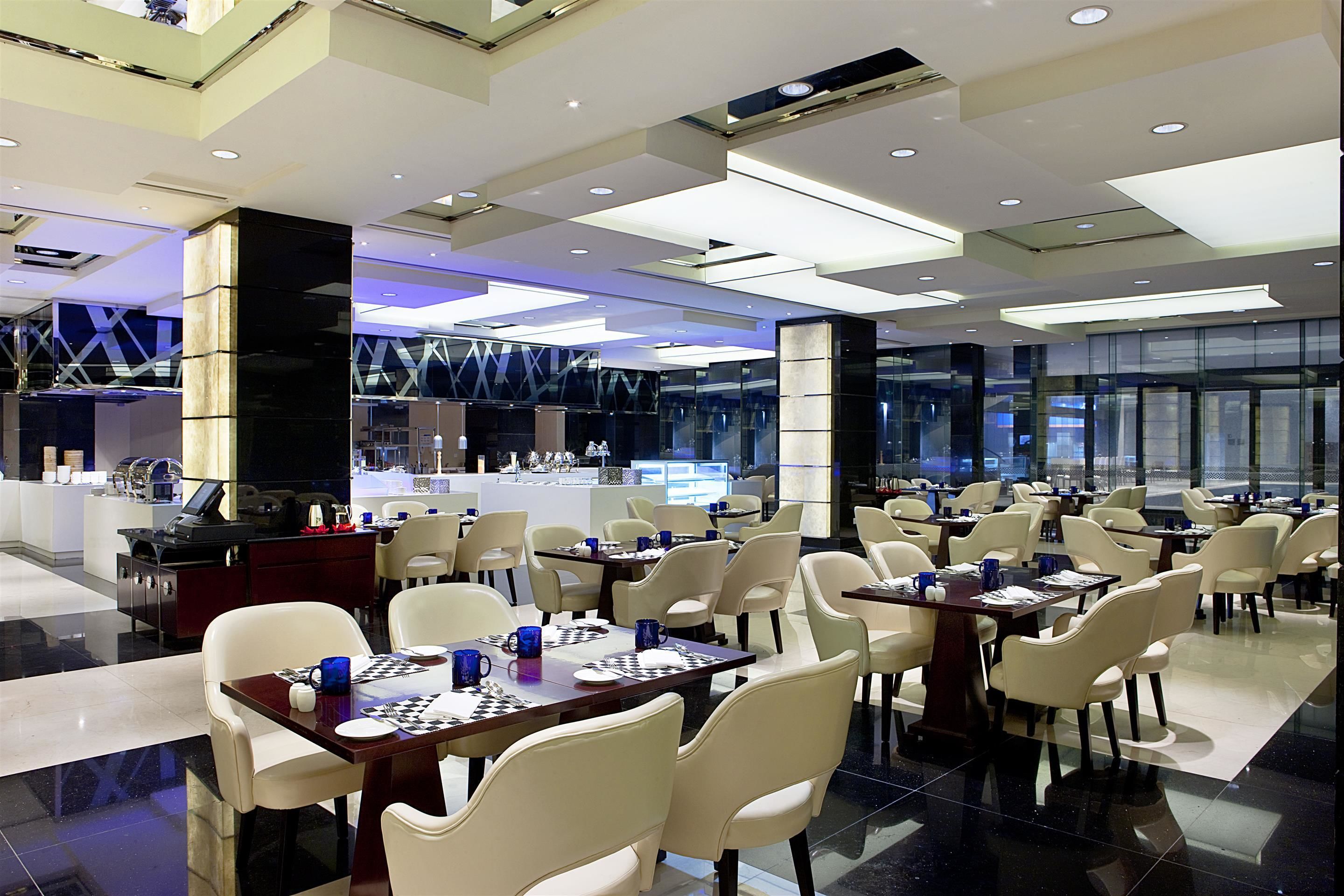 A modern dining area with multiple tables and chairs, a reception desk, and a glass partition wall.