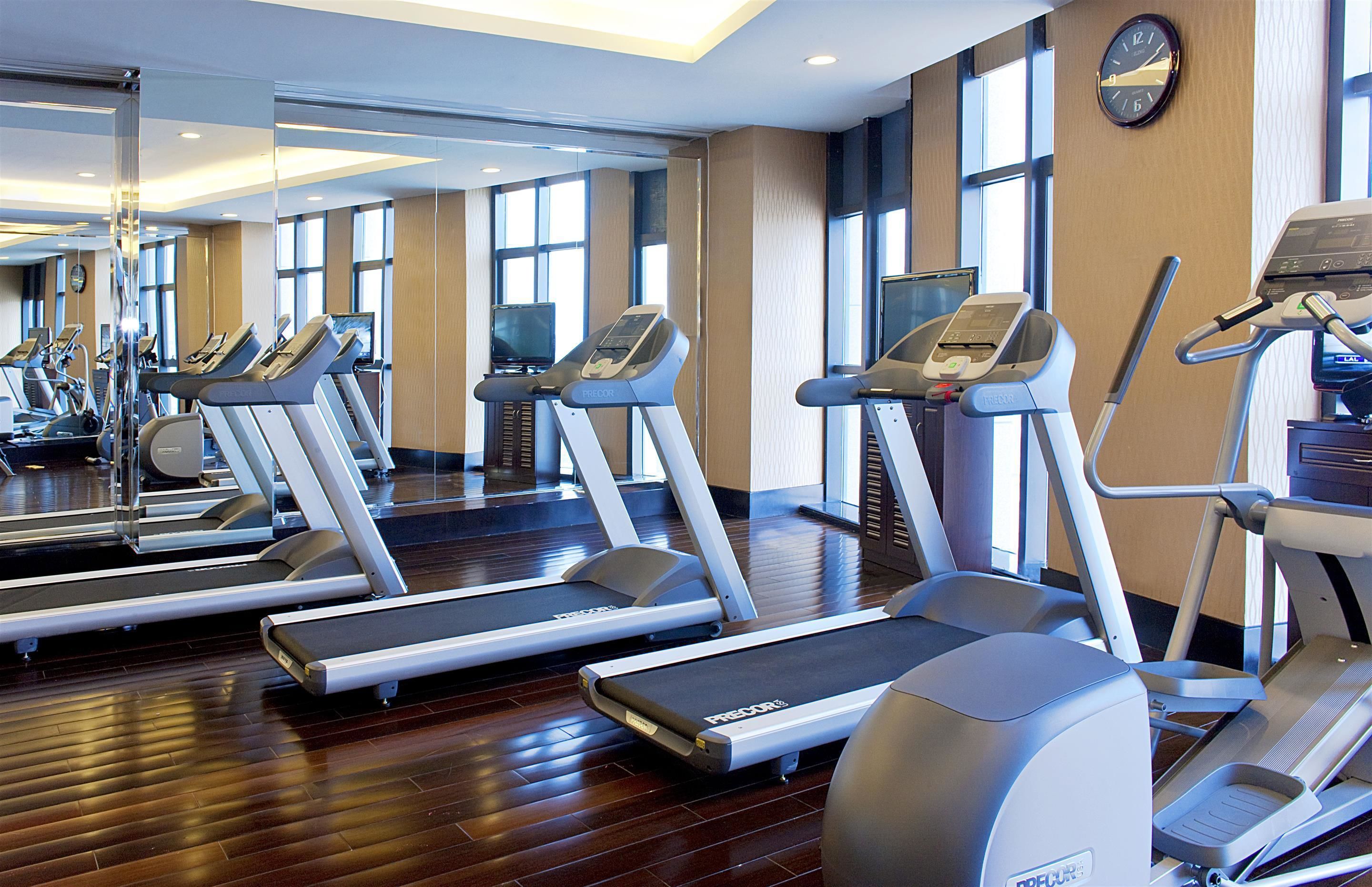 A gym with multiple treadmills, mirrors, and a clock on the wall.