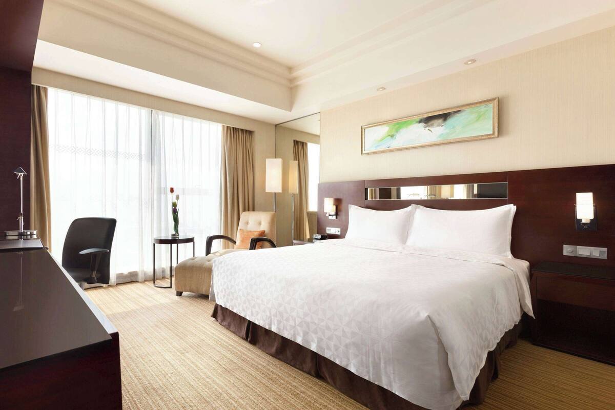 Een hotelkamer met een groot bed, een bureau, een stoel en een lamp.