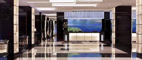Un moderno vestíbulo de hotel con piso reflectante, una gran pantalla digital mostrando una vista panorámica y un diseño contemporáneo del techo.