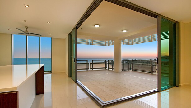 Une chambre d’hôtel moderne avec balcon, ventilateur de plafond et vue sur l’océan au coucher du soleil.