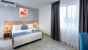 Et moderne hotelværelse med seng, sengeborde, et vindue med gardiner og et billede på væggen.