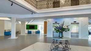 En rummelig lobby med et marmorgulv, et dekorativt bord med en vase blomster, en grøn væg med et fladskærms-tv og en balkon med udskårne gelændere.