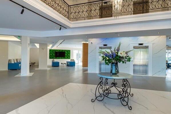 A spacious lobby with a marble floor, a decorative table with a vase of flowers, a green wall with a flat-screen TV, and a balcony with ornate railings. - Martinez (Sozopol)