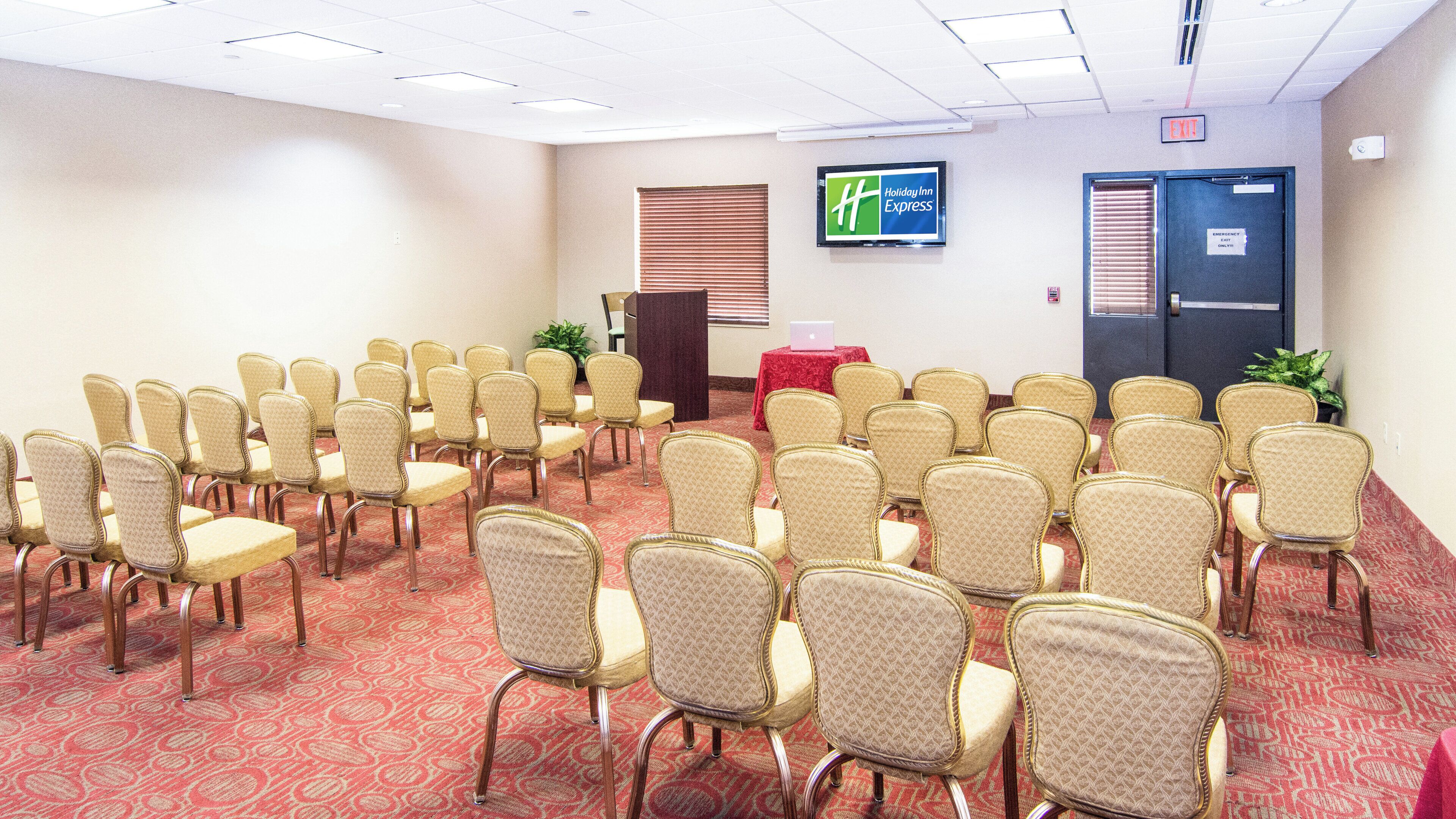 Une salle de conférence avec des rangées de chaises, un pupitre et une enseigne Holiday Inn Express.