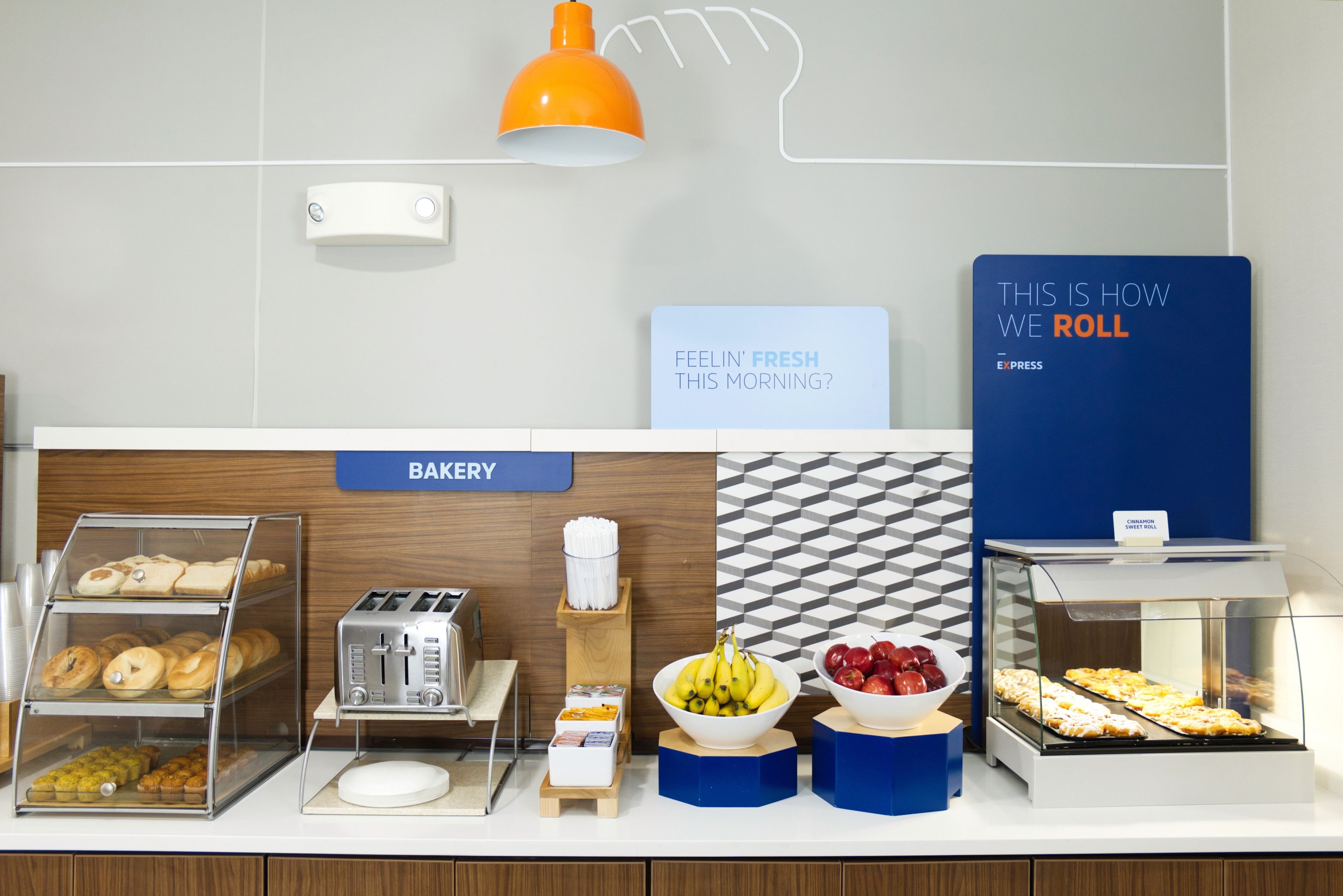 A bakery counter with various baked goods, a toaster, and a sign that reads 'THIS IS HOW WE ROLL'.