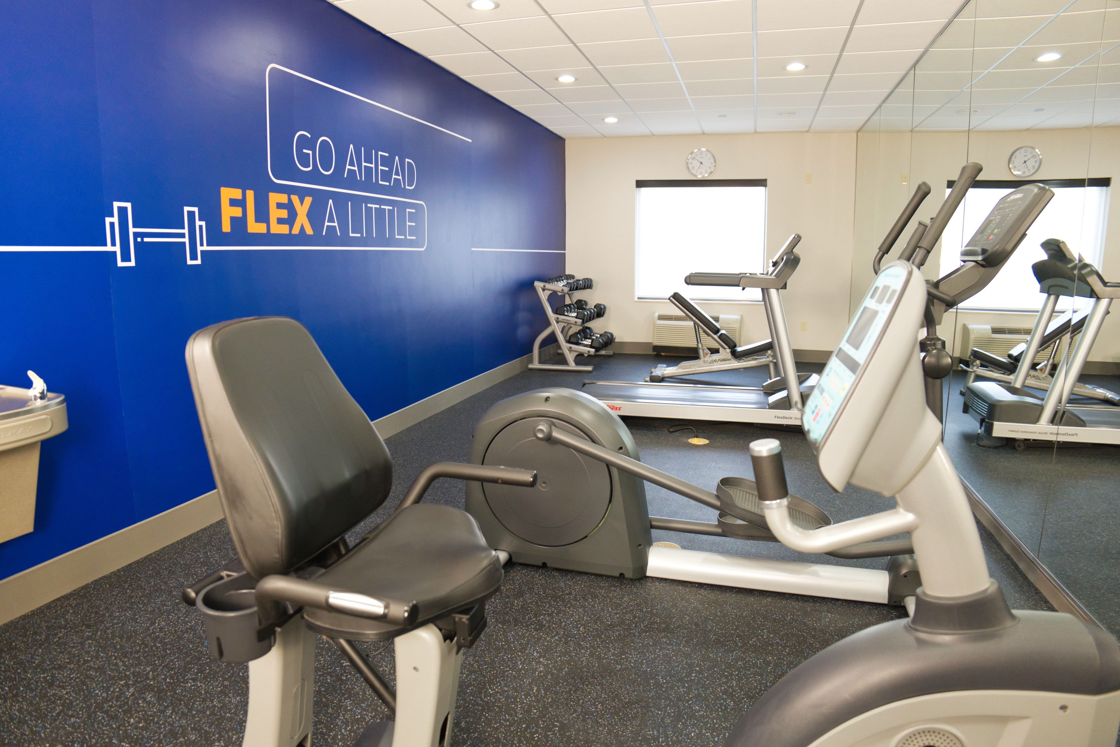 Ein Fitnessstudio mit Cardiogeräten, Krafttrainingsgeräten und einer blauen Wand mit motivierenden Texten.