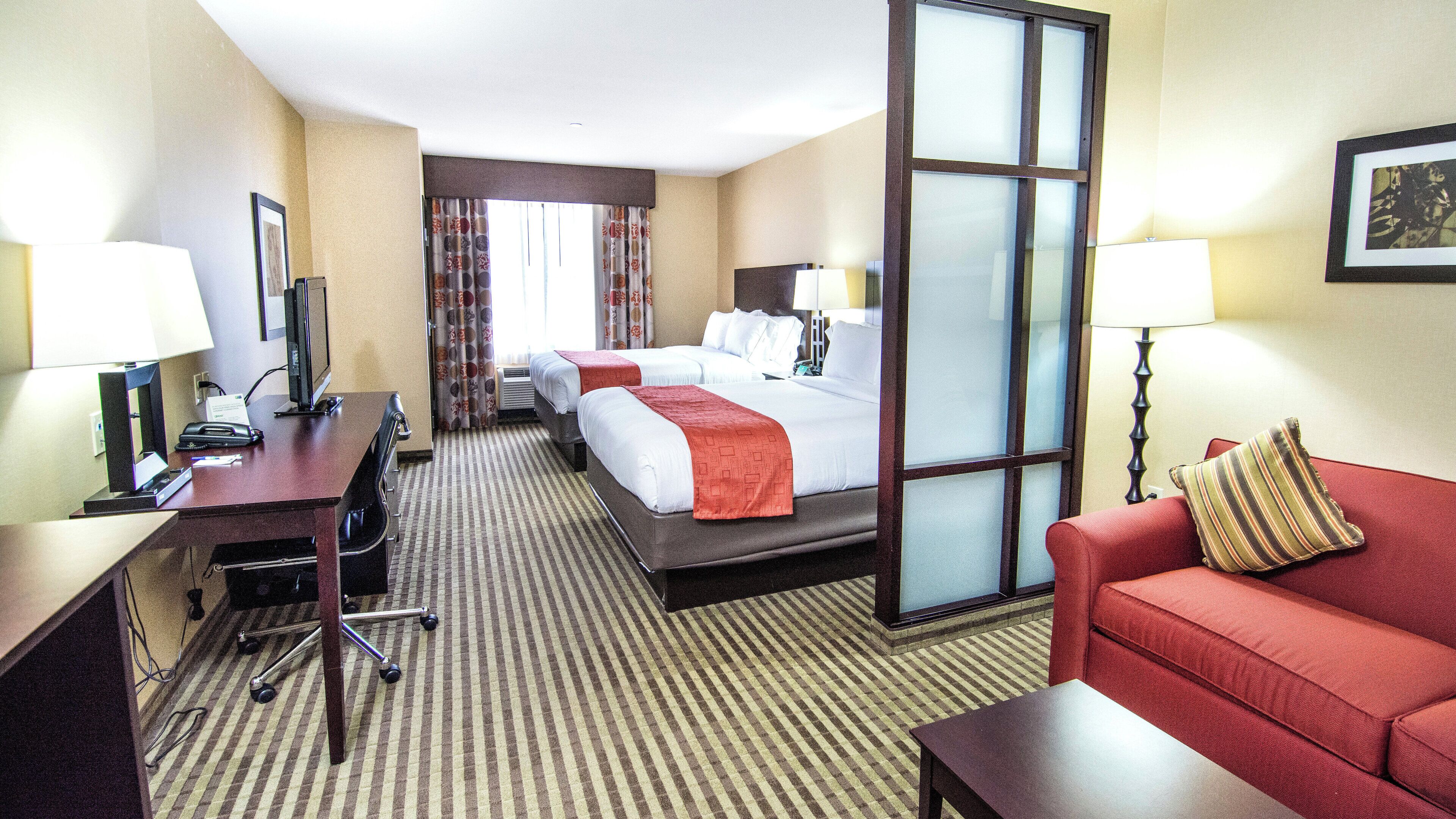 Una habitación de hotel con escritorio, dos camas, un sofá rojo y un ventanal grande.