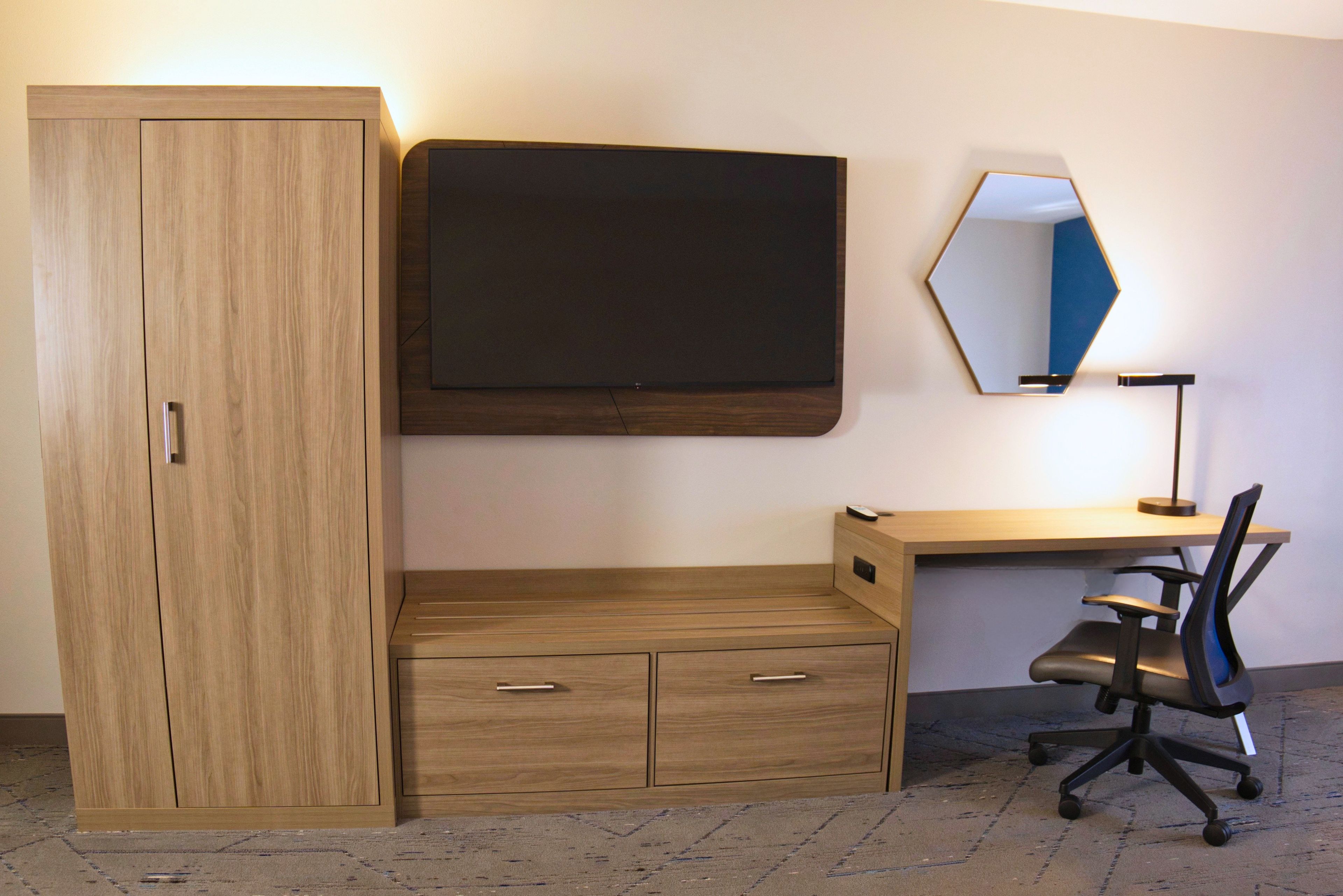 A room with a wooden wardrobe, a desk with a chair, and a wall-mounted mirror.