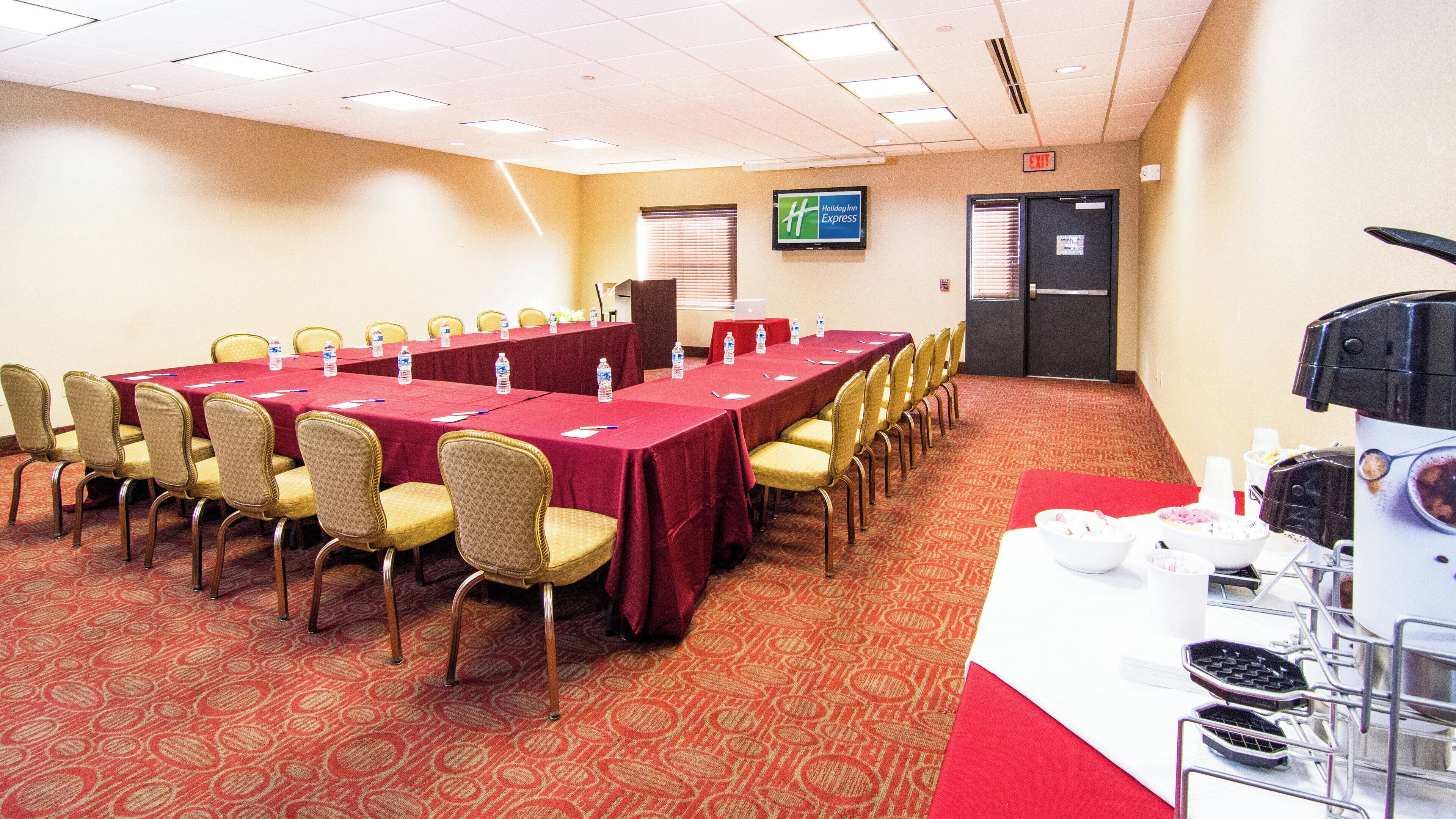 Une salle de conférence avec une longue table, des chaises et un ordinateur portable posé sur la table. On peut voir une enseigne « Holiday Inn Express » sur le mur.