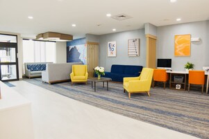 A hotel lobby with a reception desk, seating area with sofas and armchairs, a television, and artwork on the walls.