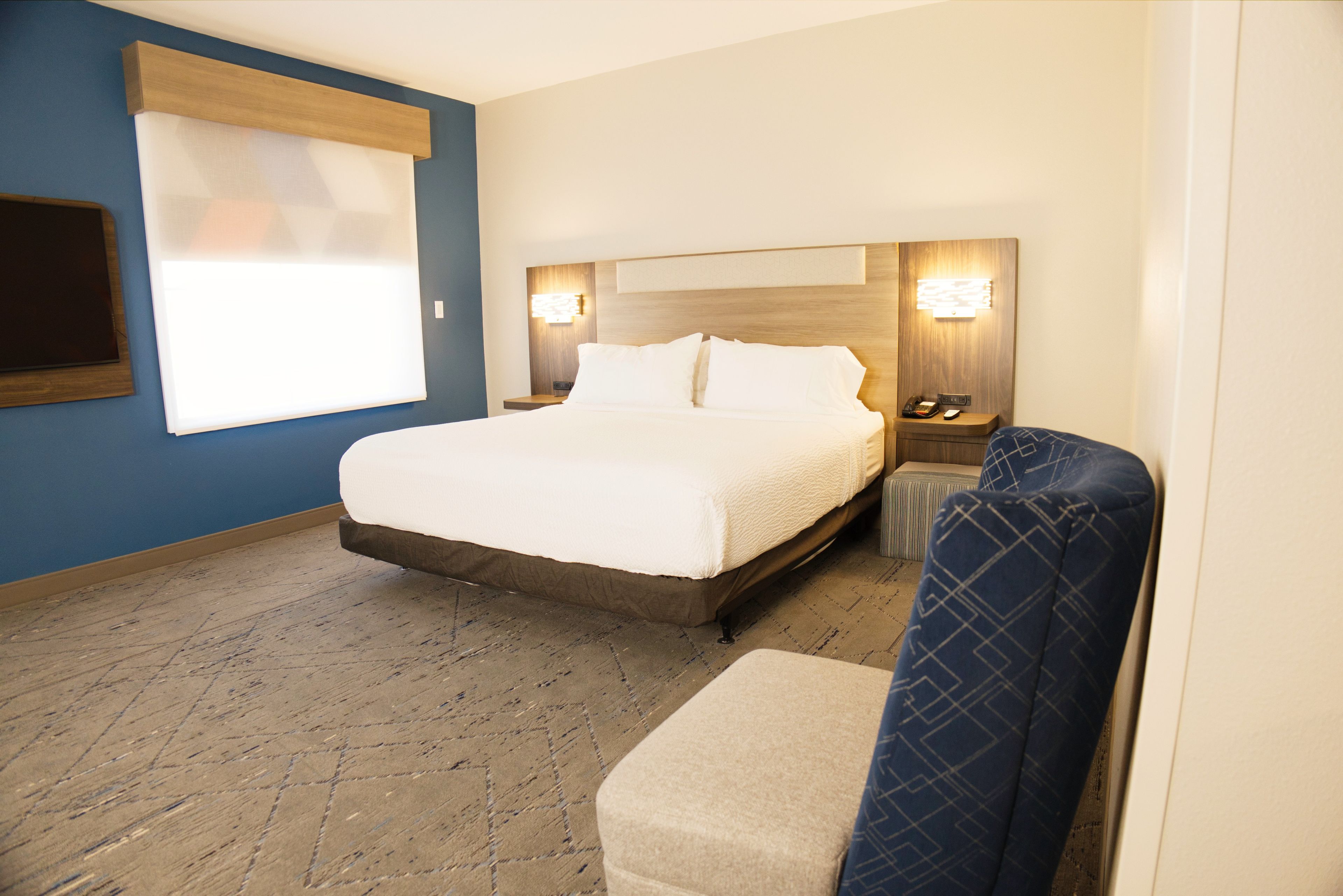 Habitación de hotel con una cama grande, mesitas de noche, una lámpara de pared y una ventana con persianas.