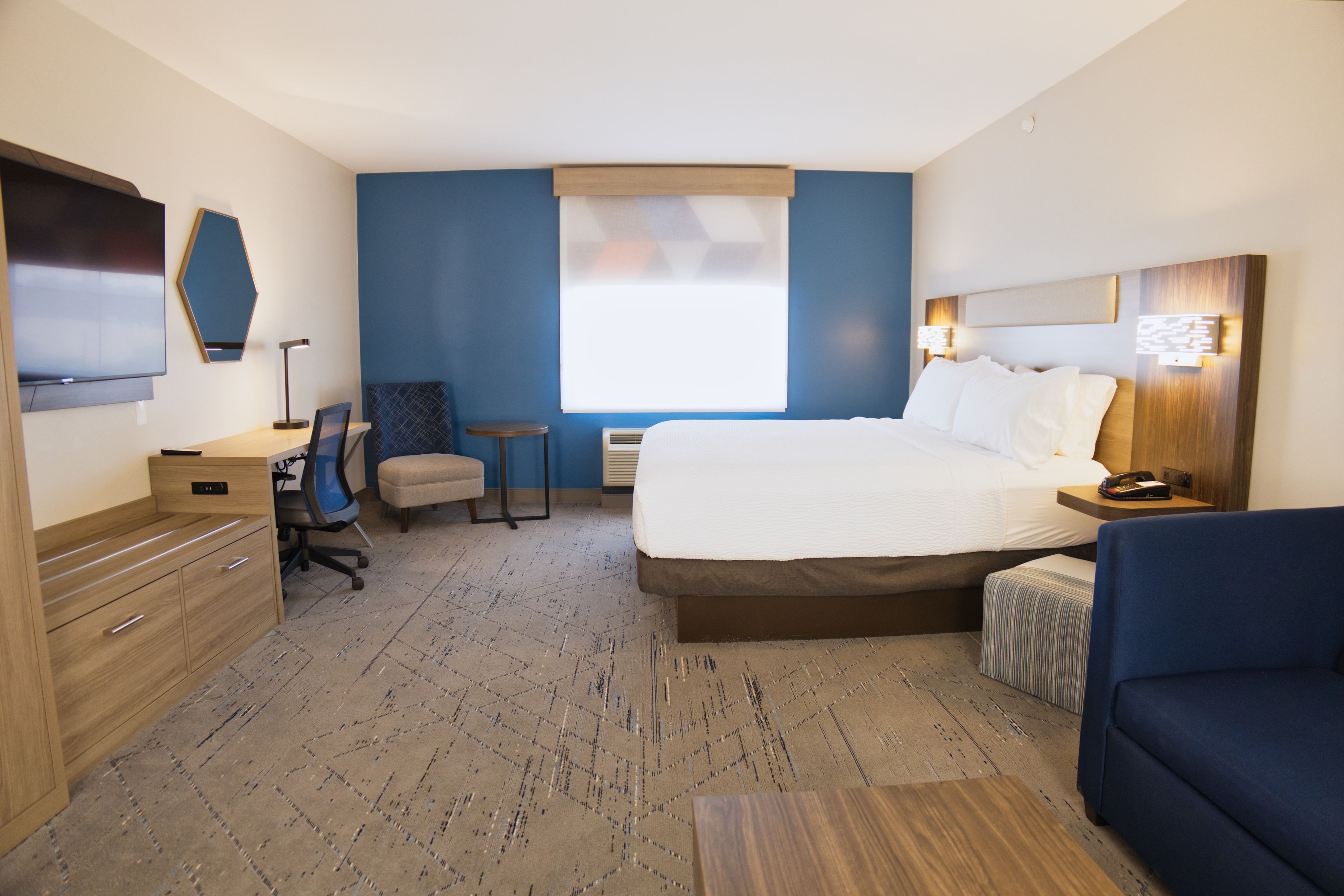 A hotel room with a bed, a desk, a chair, a TV, and a window.
