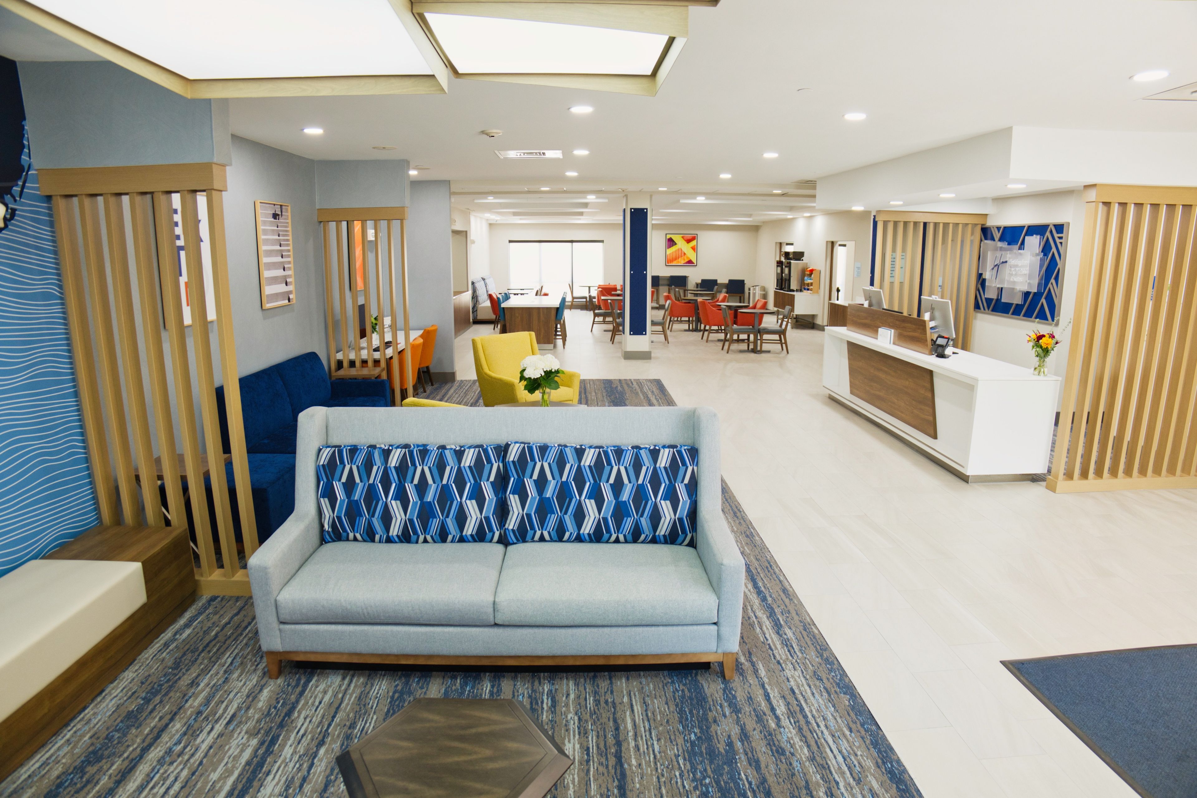 A hotel lobby with a sofa, chairs, a reception desk, and a dining area.