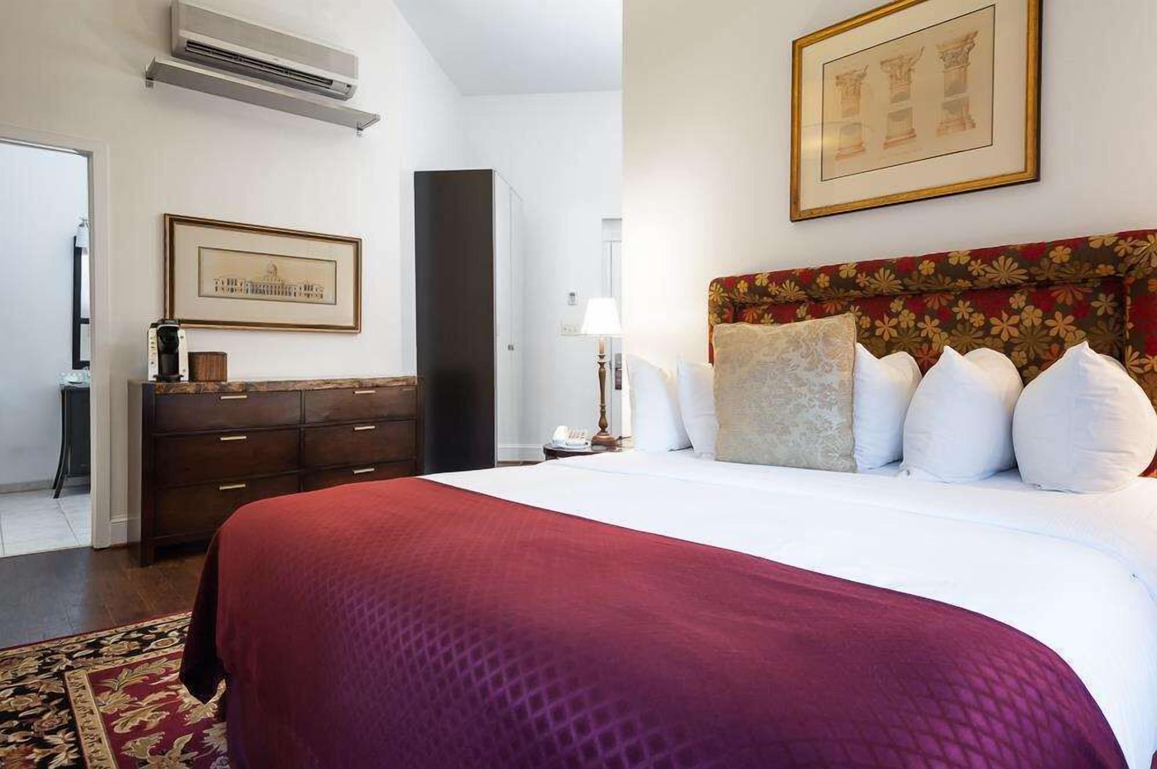A hotel room with a large bed, a dark wooden dresser, a framed picture on the wall, and a red and white patterned rug.