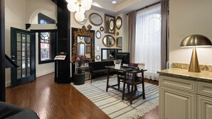 A spacious living room with hardwood floors, a black sofa, a coffee table, and a dining table. There are multiple mirrors on the walls, a chandelier, and a window with curtains. - Hotel Brexton, Trademark Collection by Wyndham (Baltimore)