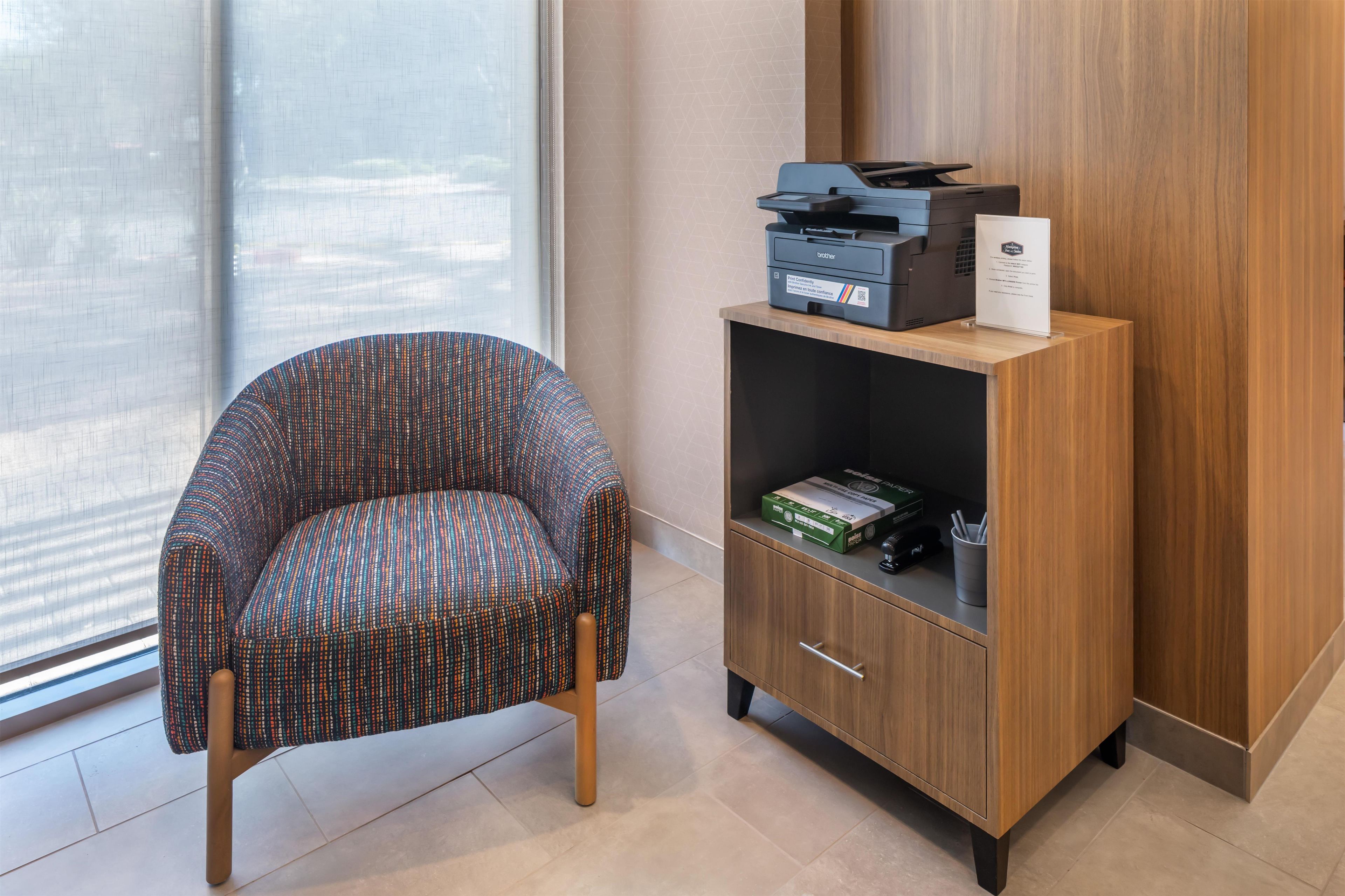 Une chaise, un meuble en bois avec une imprimante, et une fenêtre avec des stores.