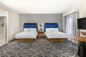 A hotel room with two beds, a small bedside table, a TV, and a bathroom.