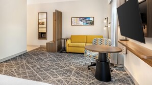 A hotel room with a sofa, a TV, a small table, a patterned rug, a side table, and a wall-mounted shelf. - Hampton Inn & Suites Riverside/Corona East (Riverside)