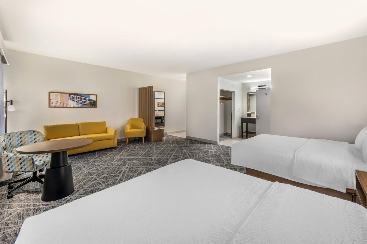 A hotel room with a bed, a sofa, a small table, a chair, and a painting on the wall.