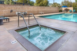 A hot tub with metal steps, a pool, and outdoor seating with chairs and tables.