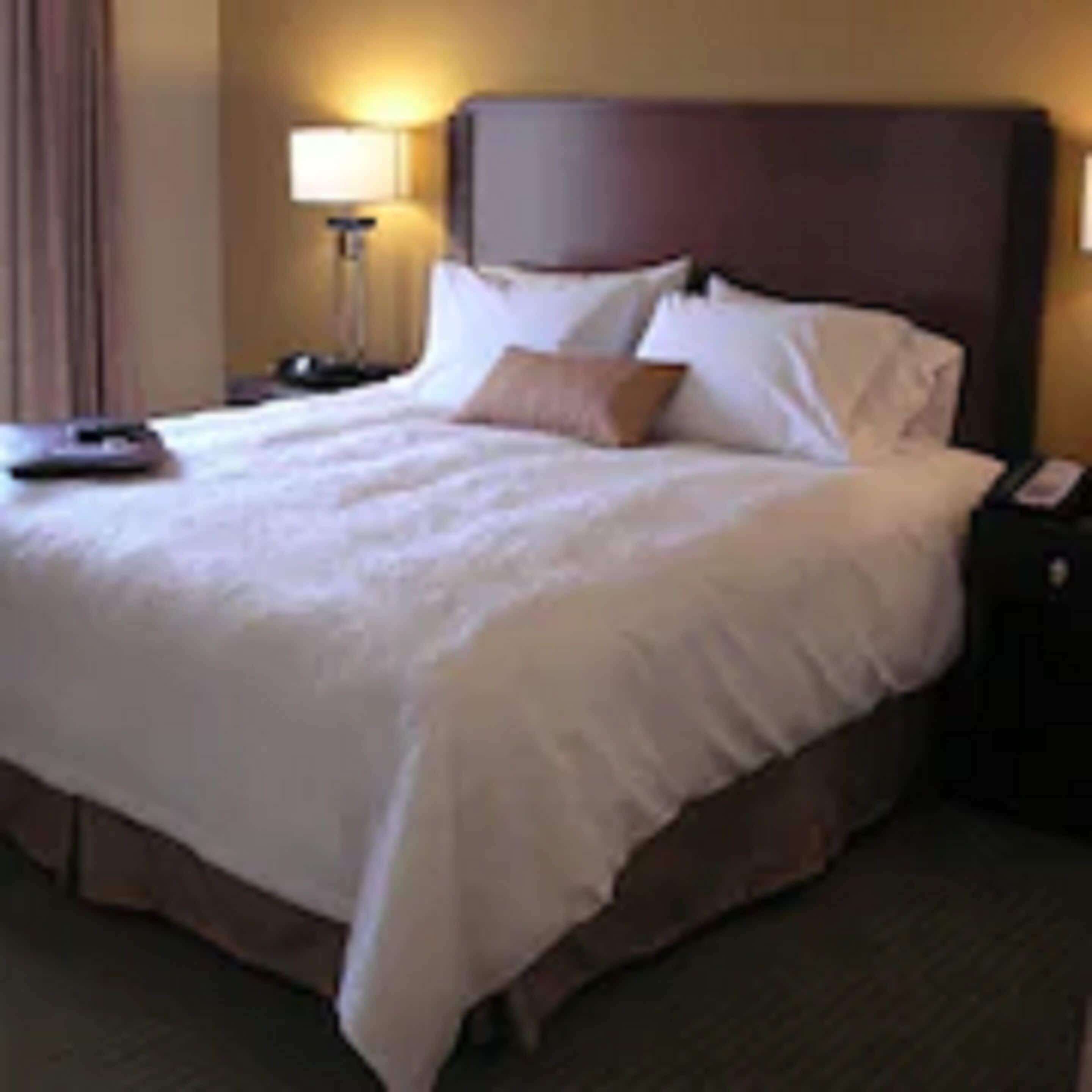 A hotel room with a large bed, a nightstand, a lamp, and a telephone.