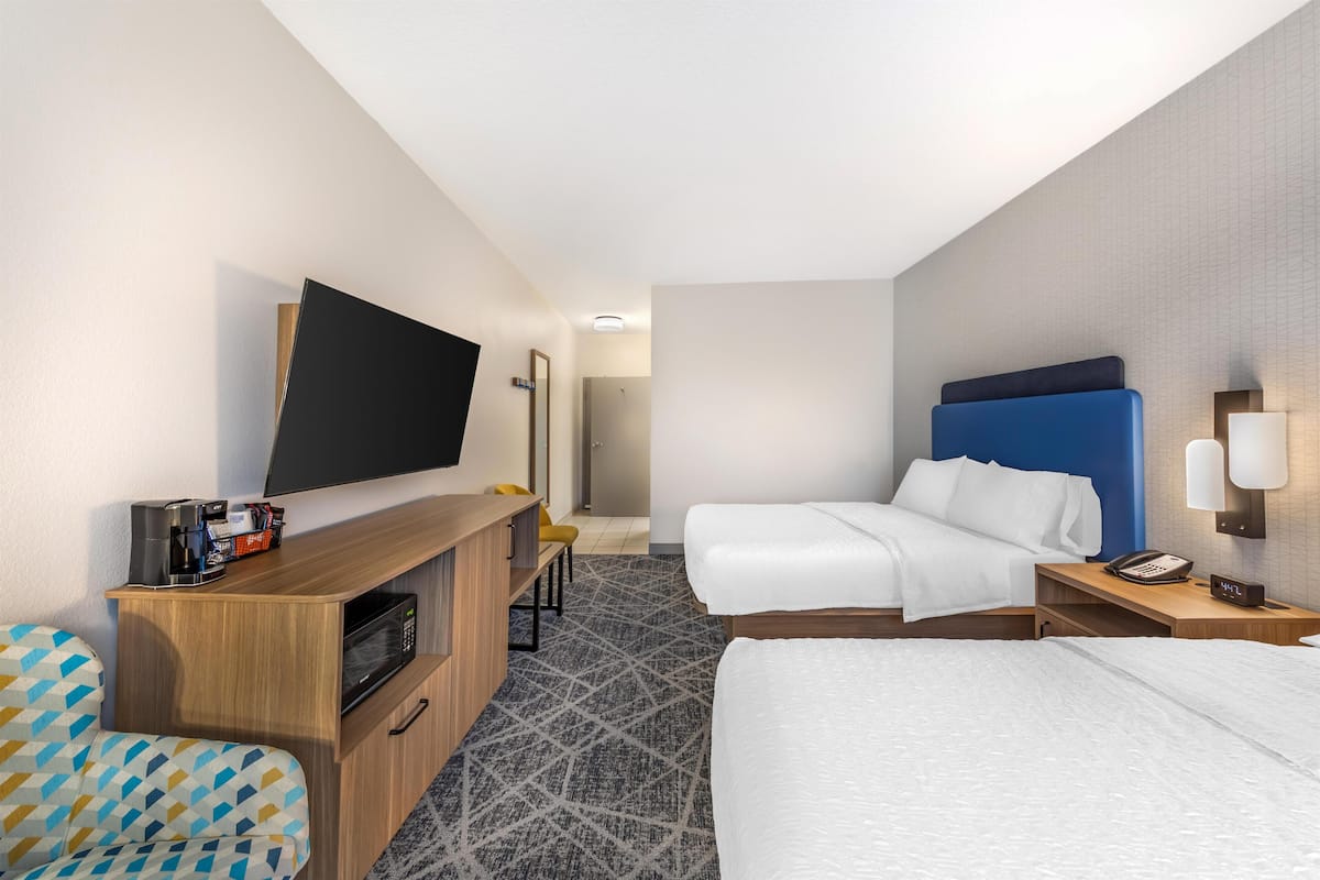 A hotel room with a flat-screen TV, two beds, a desk with a telephone, and a microwave.