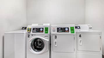 Cuatro lavadoras blancas en fila, con pantallas digitales y puertas numeradas, que señalan un lavadero automático.