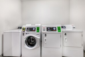 Reihe von vier weißen Wäschemaschinen mit digitalen Anzeigen und nummerierten Türen, die eine Selbstbedienungs-Wascherei kennzeichnet.