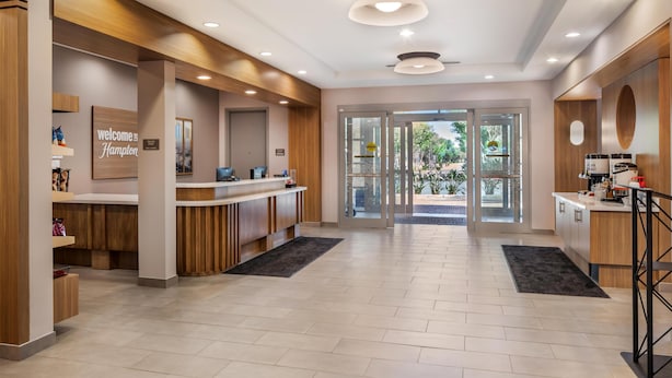 A modern hotel lobby with a reception desk, wooden accents, and a view through the glass doors. - Hampton Inn & Suites Riverside/Corona East (Riverside)