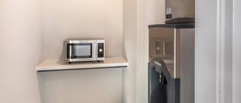 A compact kitchenette with a microwave on a shelf and a refrigerator below.