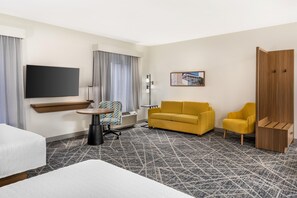 A hotel room with a bed, a sofa, a yellow armchair, a TV, a painting, and a wooden cabinet. - Hampton Inn & Suites Riverside/Corona East (Riverside)