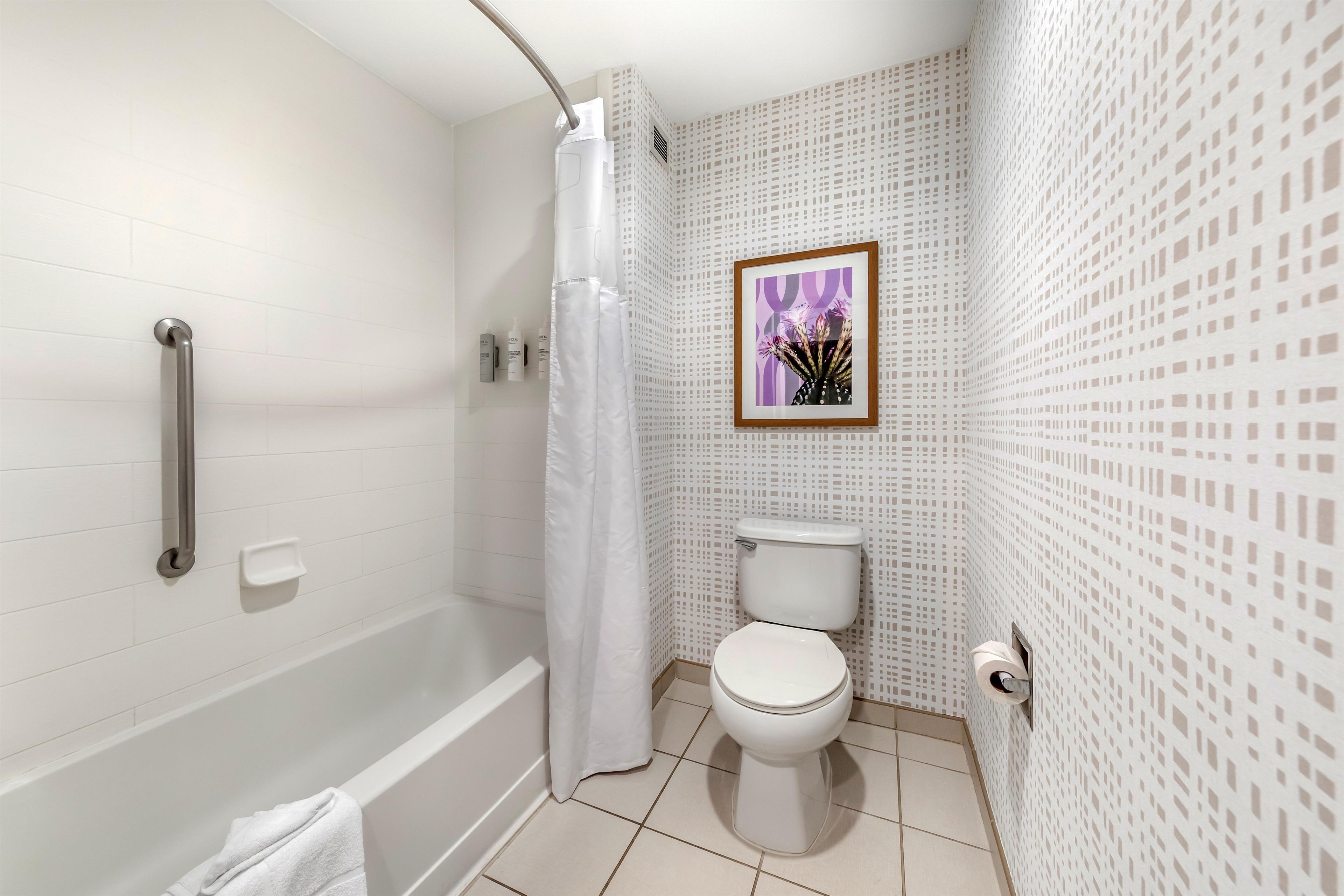A bathroom with a bathtub, toilet, shower curtain, and a framed picture on the wall.