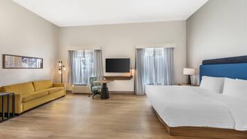 A hotel room with a bed, a sofa, a desk, a chair, a TV, and curtains.