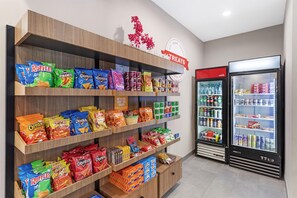 Ein Verkaufsregal mit verschiedenen Chips und Snacks, ein Schild für Leckereien und ein Kühlschrank für gekühlte Getränke.