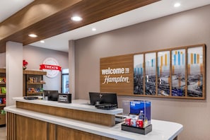 A hotel reception desk with a 'Welcome to Hampton' sign, a 'Treats' sign, and a display of beverages. - Hampton Inn & Suites Riverside/Corona East (Riverside)