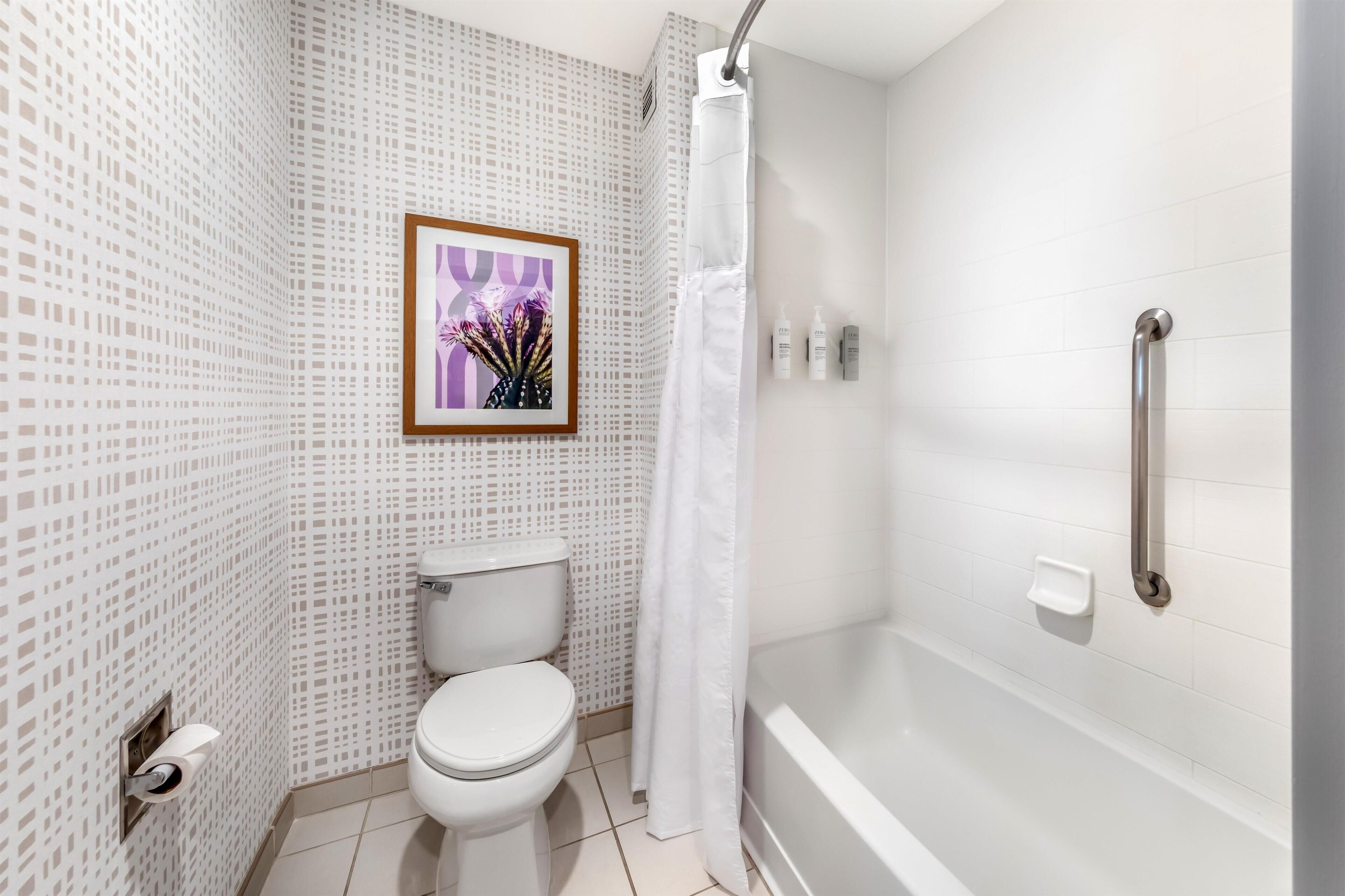 A bathroom with a toilet, shower, and a framed picture on the wall.