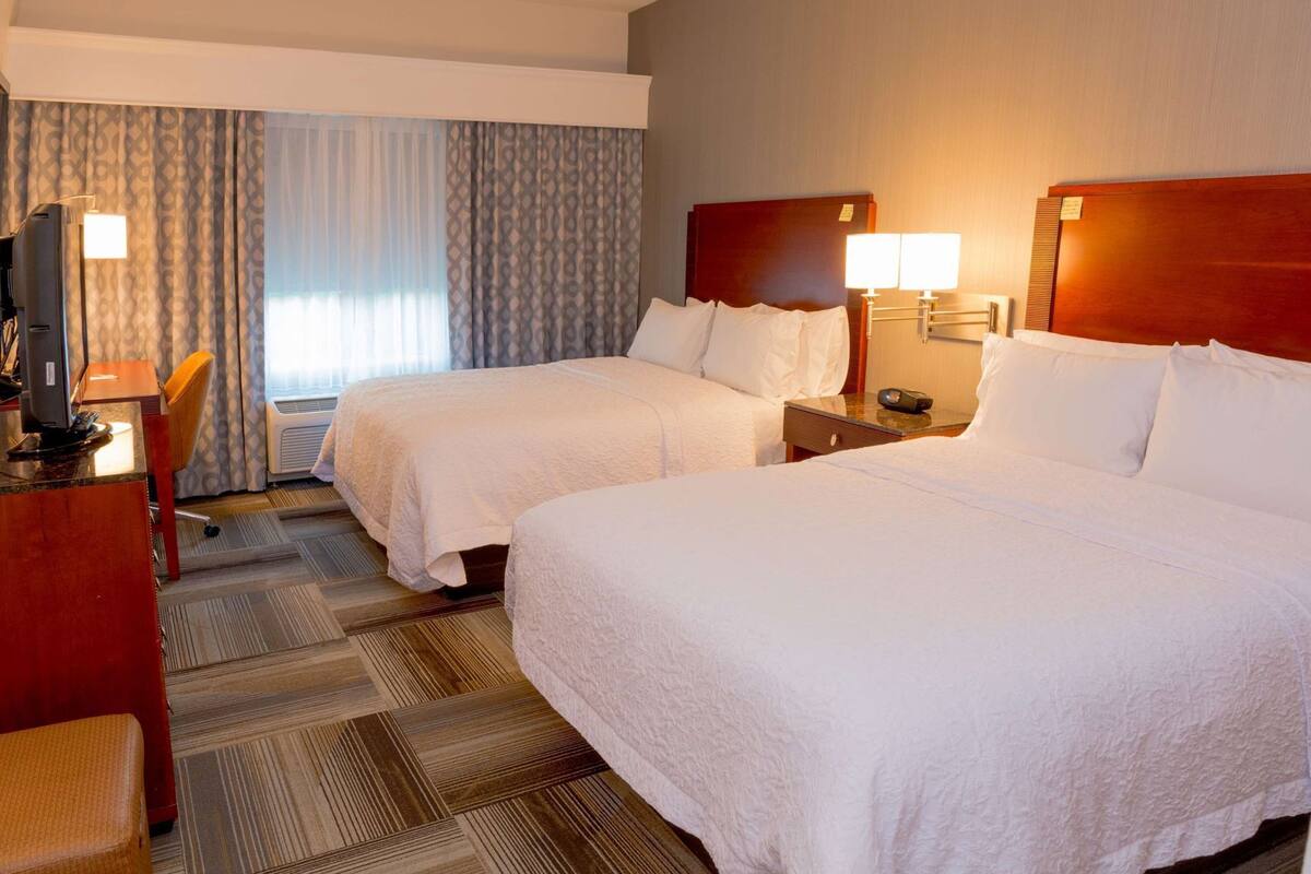 A hotel room with two beds, a desk with a computer, and a chair.