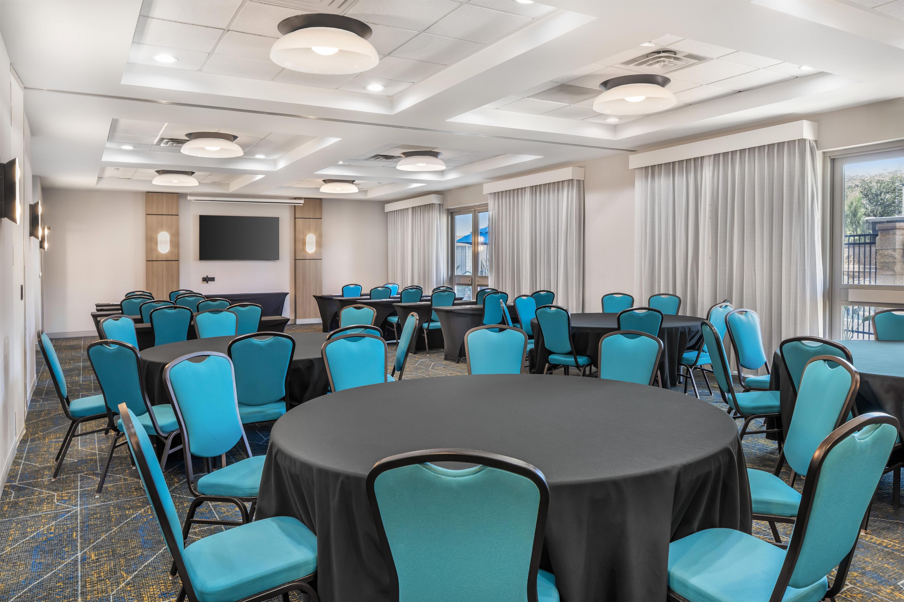 A conference room with round tables, blue chairs, a large screen, and a view of the outdoors.