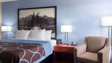 A hotel room with a bed, a desk, a chair, a nightstand, a lamp, and a large framed picture on the wall.