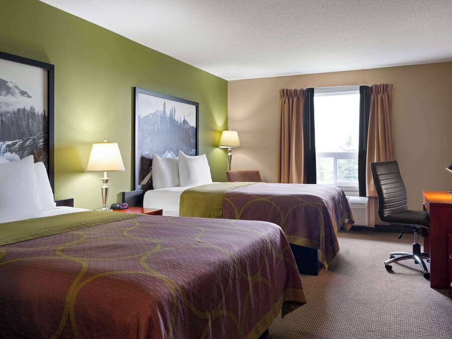 A hotel room with two beds, a desk, a chair, and a window with curtains.