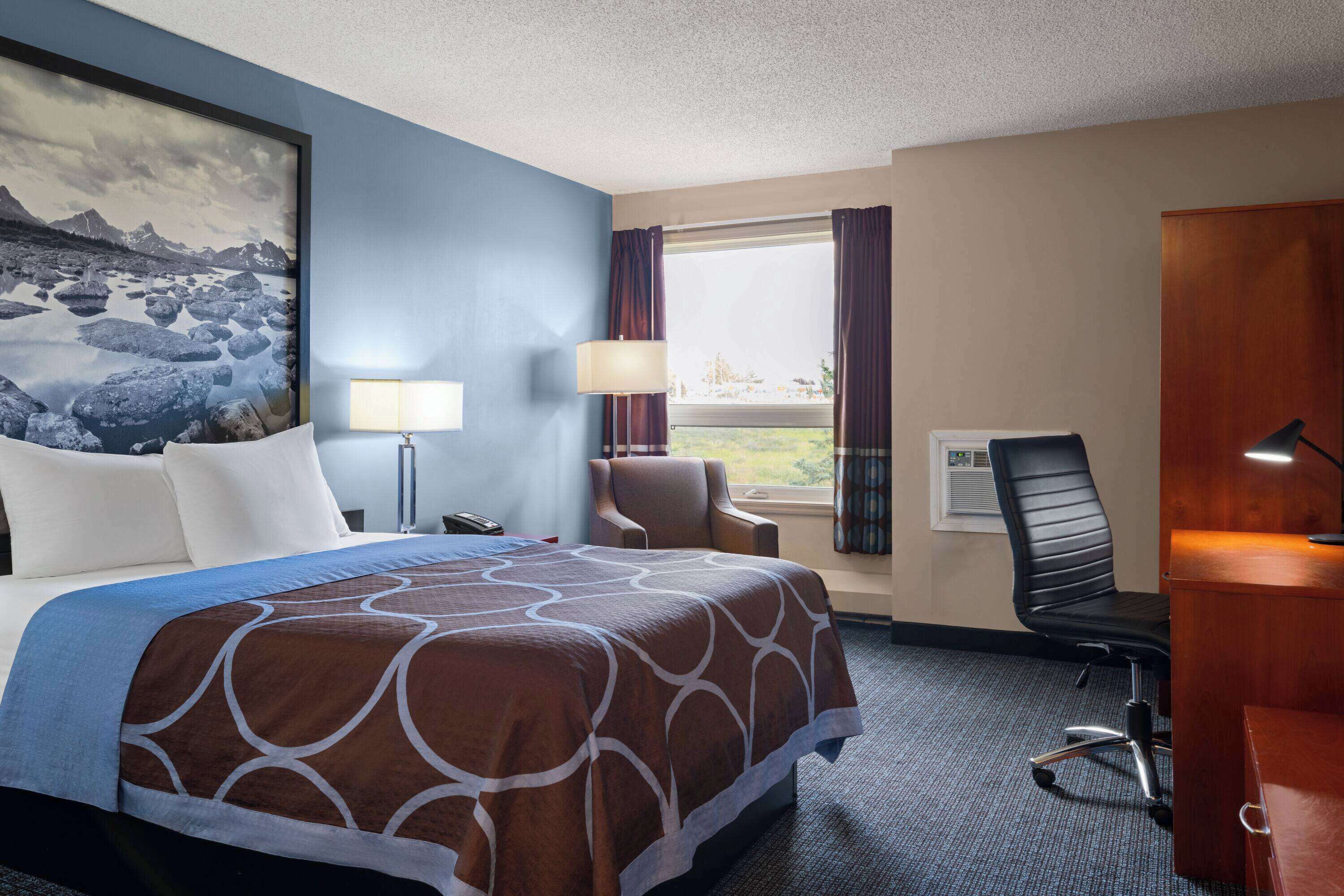 A hotel room with a bed, a desk, a chair, a lamp, and a window with curtains.