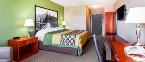 A hotel room with a bed, a desk, a chair, a TV, and a door.
