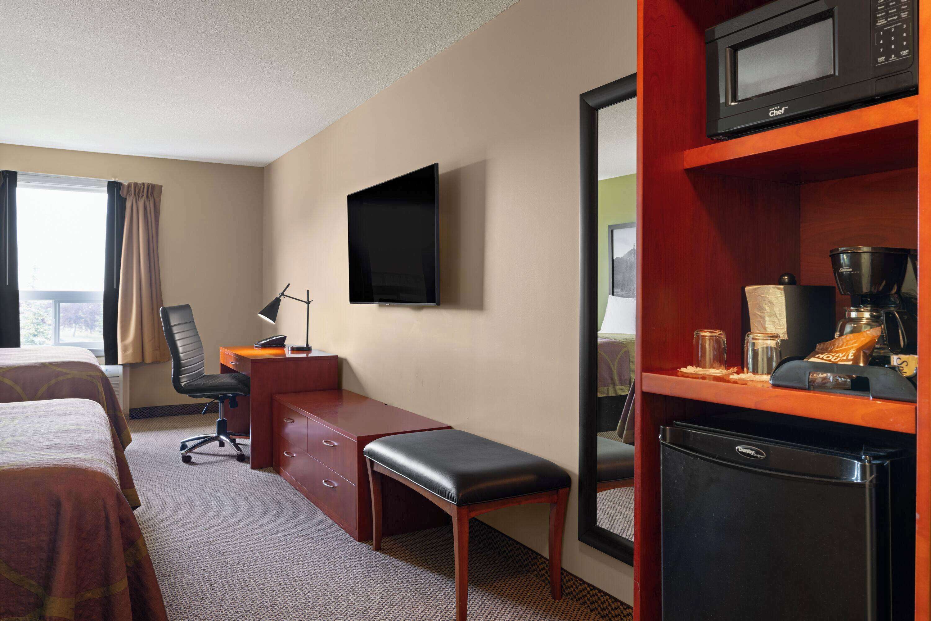 A hotel room with two beds, a desk with a chair, a television, a microwave, and a refrigerator.