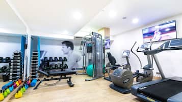 Ein Fitnessstudio mit unterschiedlichen Trainingsgeräten, Laufband und einem Fernsehbildschirm, der ein Sportevent zeigt.