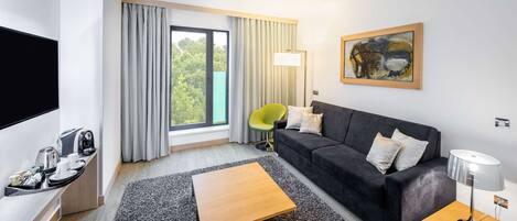 Una habitación de hotel moderna con televisión de pantalla plana, un sofá, una mesita de café, una lámpara y un cuadro en la pared.