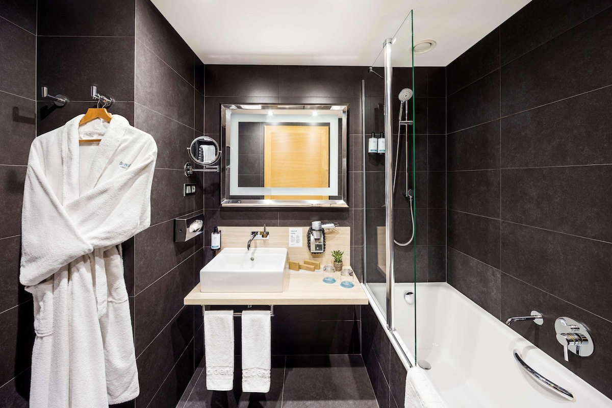 A modern bathroom with a bathtub, a sink, a mirror, and a towel rack.
