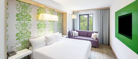 Habitación de hotel con una cama grande, un sofá, un televisor y un ventanal con cortinas.