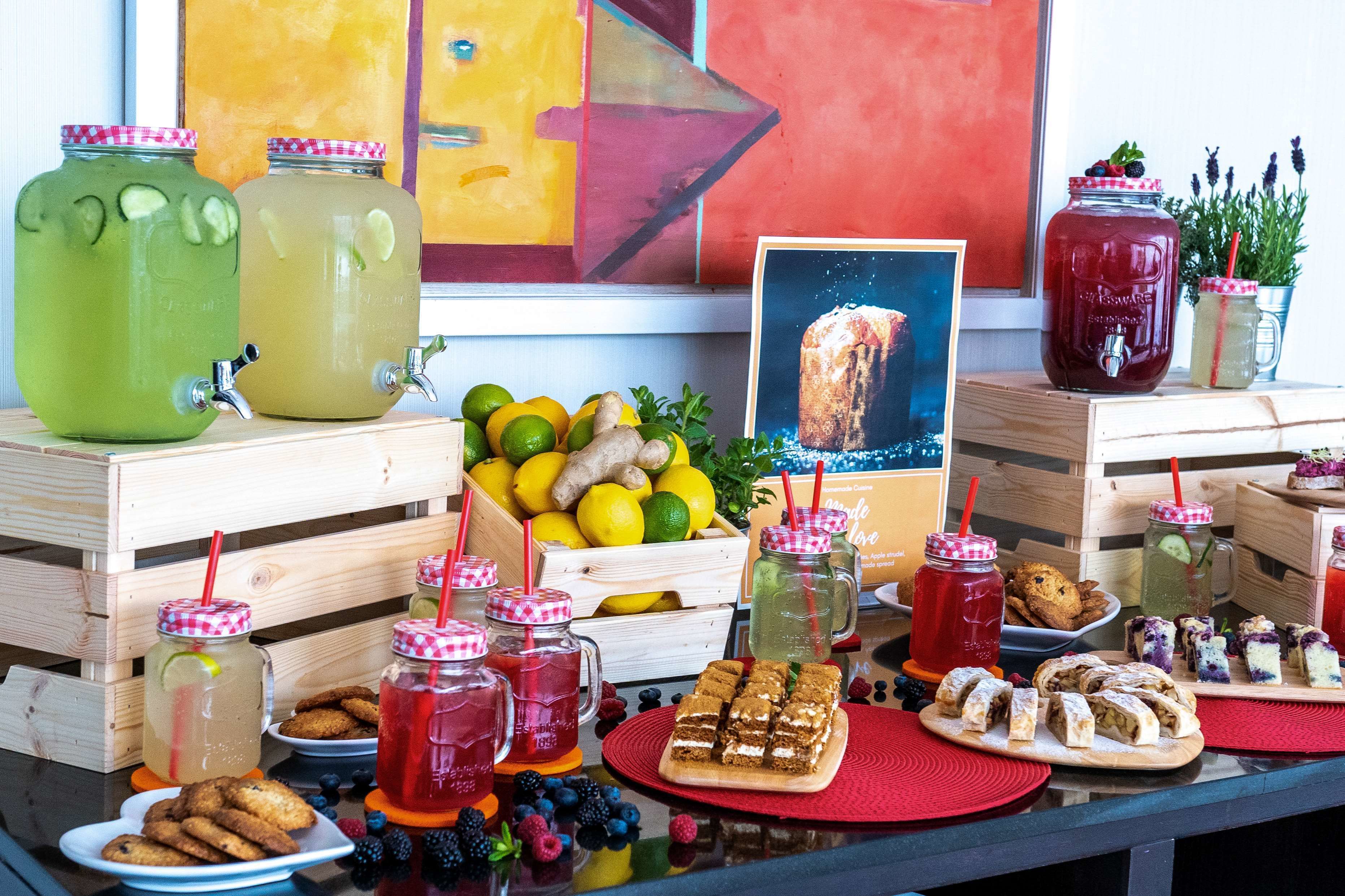 Una mesa con diversos alimentos, bebidas y un cuadro.