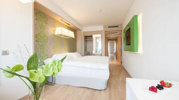 Una habitación de hotel con una cama, una mesita de noche con fruta, un jarrón con plantas y una pared verde.